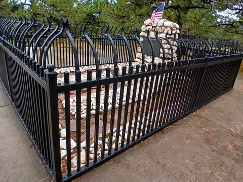 Buffalo Bill's grave on Lookout Mountain: a white stone cairn with a bronze plaque and a small flag, inside a black iron fence under pines