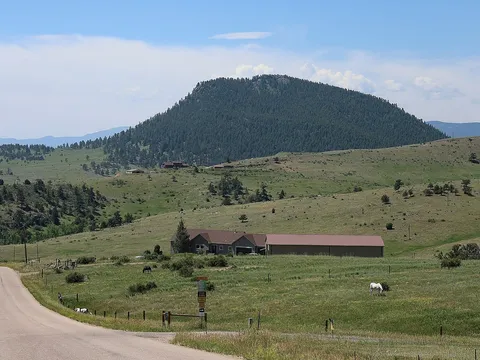 The forested dome of Centennial Cone seen from Camino Perdido, with ranch meadows and grazing horses in front