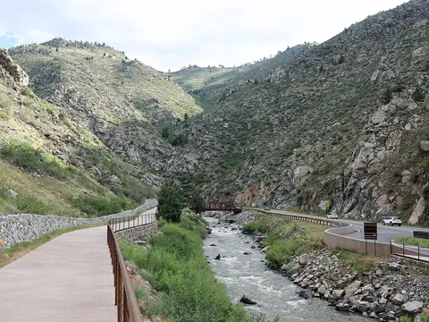 Clear Creek Canyon Park at the CCR Trailhead: the paved trail on the left, the creek and a footbridge in the middle and US 6 on the right between rocky canyon walls