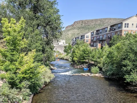 Tubers riding a drop on Clear Creek just below the Washington Avenue bridge, with South Table Mountain behind