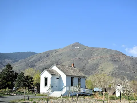 The white 1876 Guy Hill schoolhouse in Golden History Park, with the M of Mount Zion on the hillside behind
