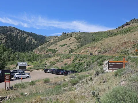 The Mount Galbraith Park trailhead on Golden Gate Canyon Road: the park sign, the gravel parking lot and restroom, and the foothills rising behind