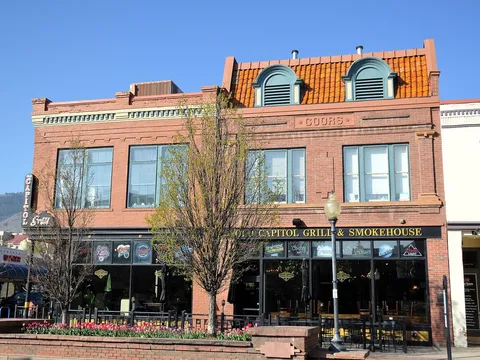 The brick frontage of Old Capitol Grill & Smokehouse on Washington Avenue, its name over the windows and patio tables and tulips in front